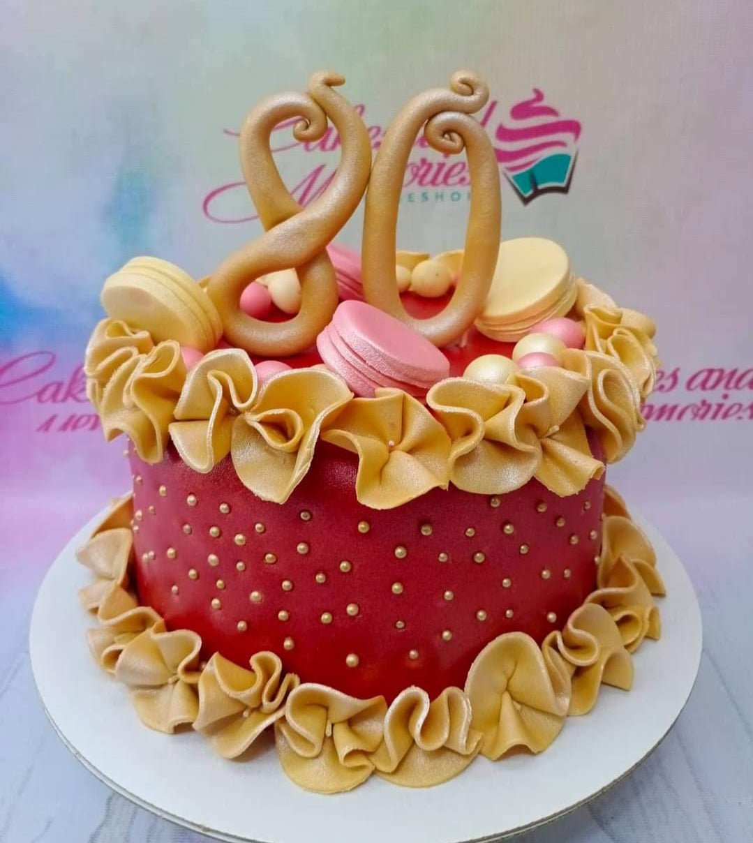 Red 80th birthday cake with gold ruffles, gold number 80 topper, pink and cream macarons, and gold dragees. Red 80th birthday cake with gold ruffles, gold number 80 topper, pink and cream macarons, and gold dragees.