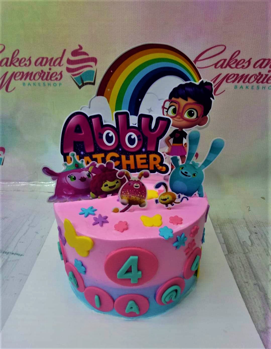 Pink Abby Hatcher themed birthday cake with rainbow and character printouts, featuring colorful fondant butterflies and flowers. Pink Abby Hatcher themed birthday cake with rainbow and character printouts, featuring colorful fondant butterflies and flowers.