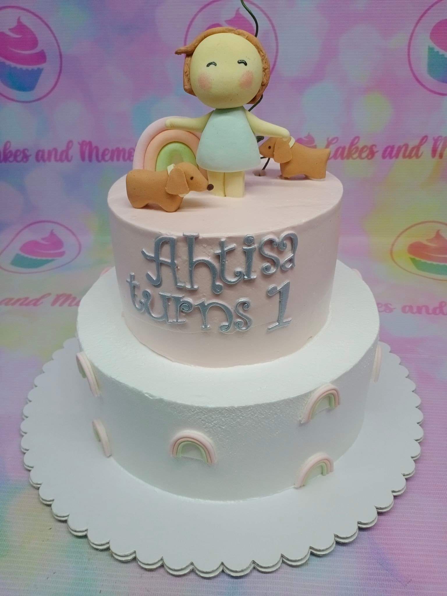 Two-tier pink and white birthday cake with a fondant girl figure, dogs, and rainbows. Two-tier pink and white birthday cake with a fondant girl figure, dogs, and rainbows.