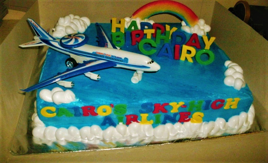 Blue rectangular airplane themed birthday cake with a large toy airplane, rainbow topper, and white icing clouds. Blue rectangular airplane themed birthday cake with a large toy airplane, rainbow topper, and white icing clouds.