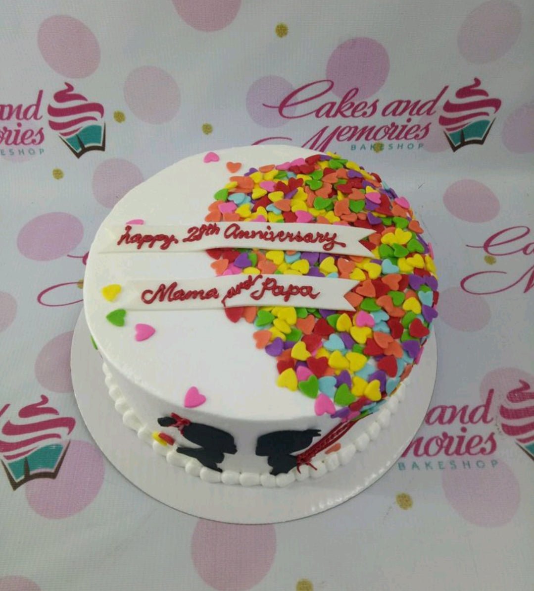 White round anniversary cake with a colorful heart made of small fondant hearts and two white banners with red icing text. White round anniversary cake with a colorful heart made of small fondant hearts and two white banners with red icing text.