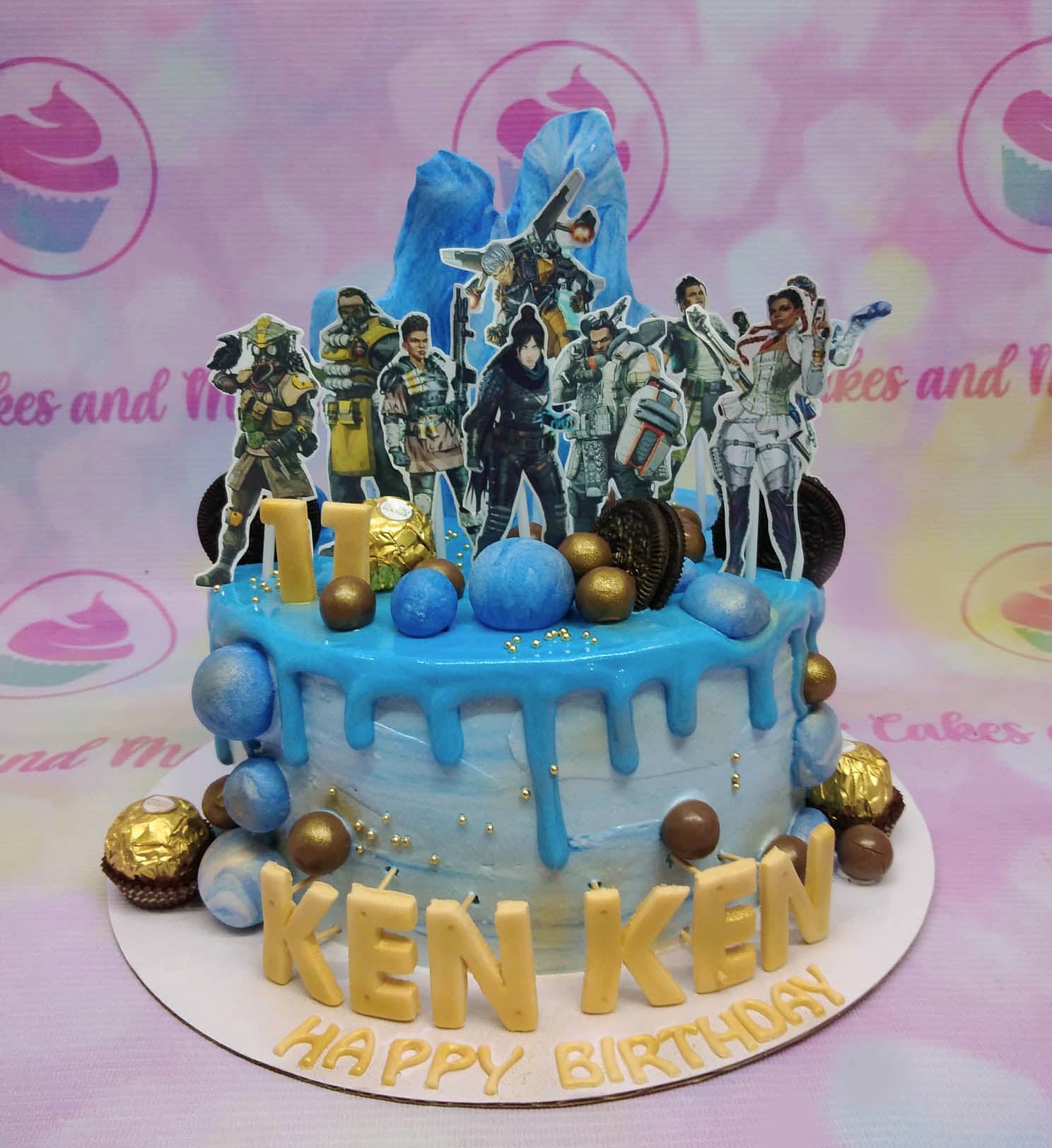 Blue Apex Legends themed birthday cake with character printouts, blue icing drip, and gold chocolate accents. Blue Apex Legends themed birthday cake with character printouts, blue icing drip, and gold chocolate accents.