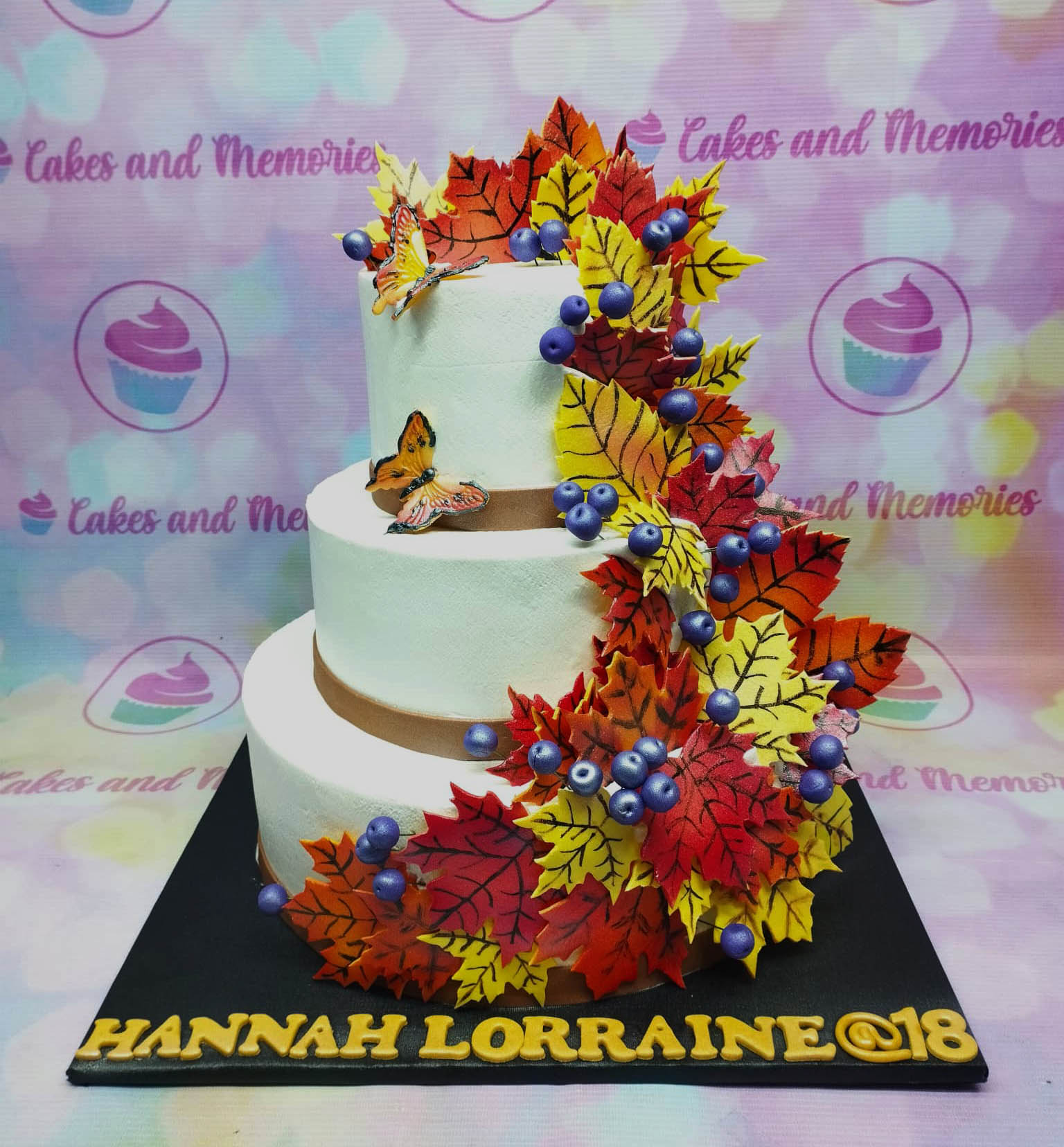 Three-tier white autumn-themed cake decorated with vibrant red, orange, and yellow maple leaves and purple berries. Three-tier white autumn-themed cake decorated with vibrant red, orange, and yellow maple leaves and purple berries.