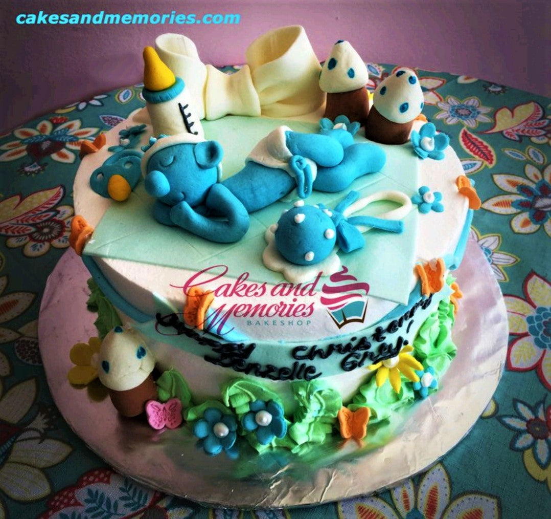Blue baby boy sleeping on a light blue fondant blanket with baby bottle, rattle, and pacifier toppers on a white and blue cake. Blue baby boy sleeping on a light blue fondant blanket with baby bottle, rattle, and pacifier toppers on a white and blue cake.