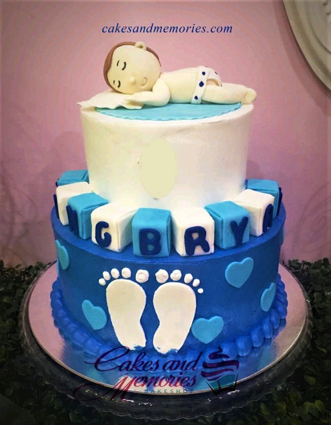 Two-tier blue and white baby shower cake with a sleeping fondant baby topper and blue block letters. Two-tier blue and white baby shower cake with a sleeping fondant baby topper and blue block letters.