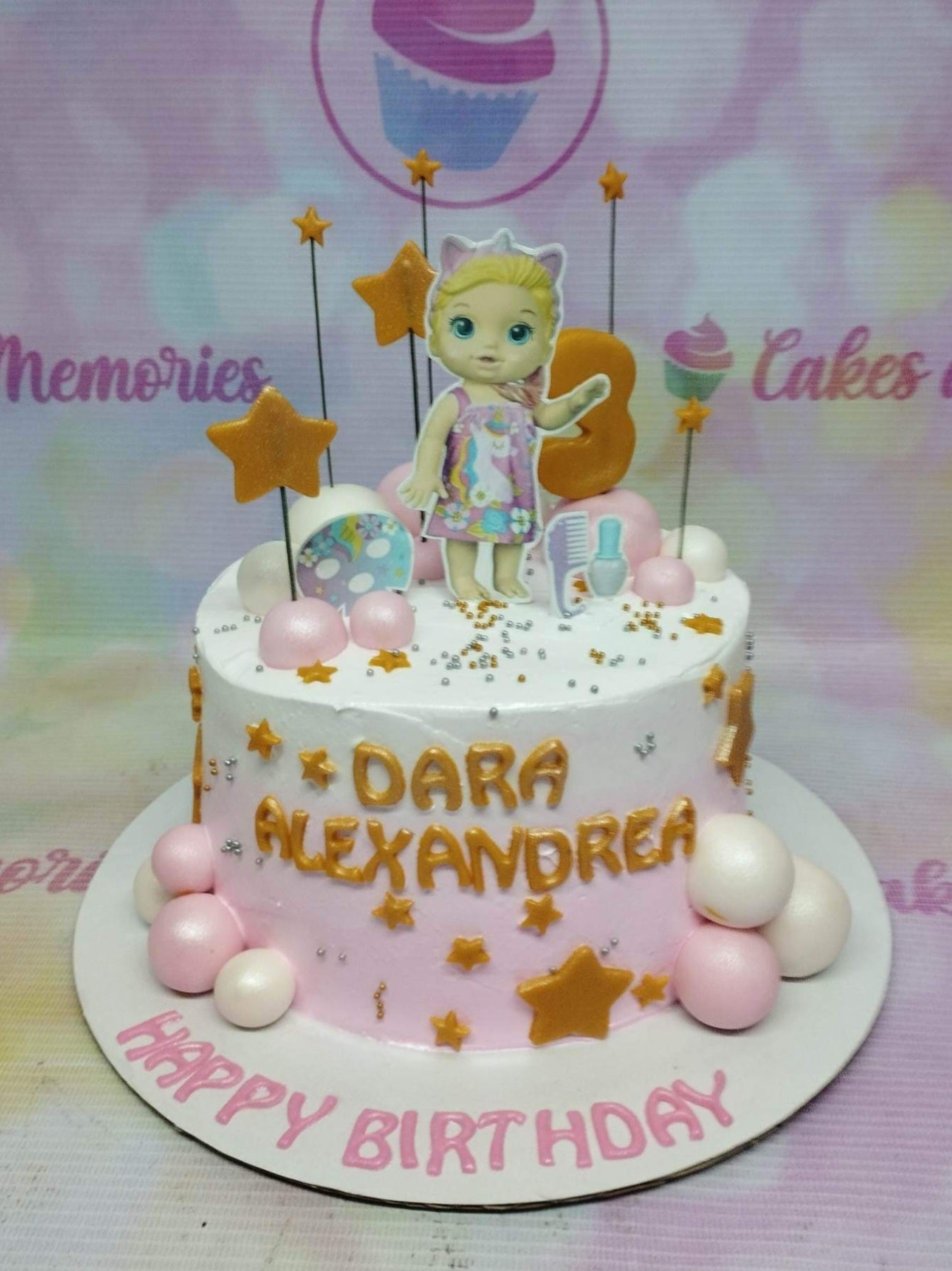 Pink and white baby doll themed birthday cake with gold stars, pink spheres, and a character printout topper. Pink and white baby doll themed birthday cake with gold stars, pink spheres, and a character printout topper.