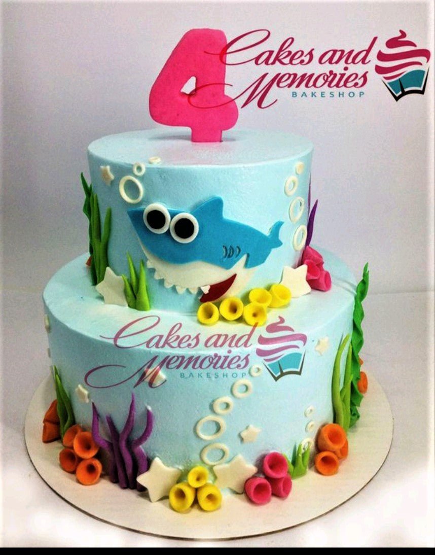 Two-tier light blue Baby Shark themed birthday cake with underwater fondant decorations like coral, seaweed, and a pink number 4 topper. Two-tier light blue Baby Shark themed birthday cake with underwater fondant decorations like coral, seaweed, and a pink number 4 topper.