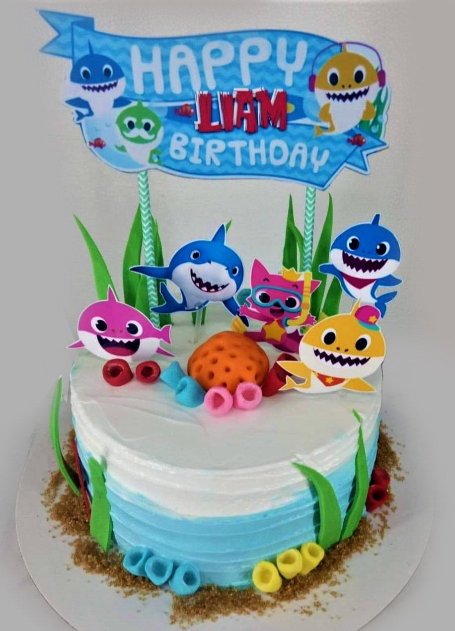 Baby Shark themed birthday cake with blue and white ombre icing, character printouts, and fondant sea elements. Baby Shark themed birthday cake with blue and white ombre icing, character printouts, and fondant sea elements.