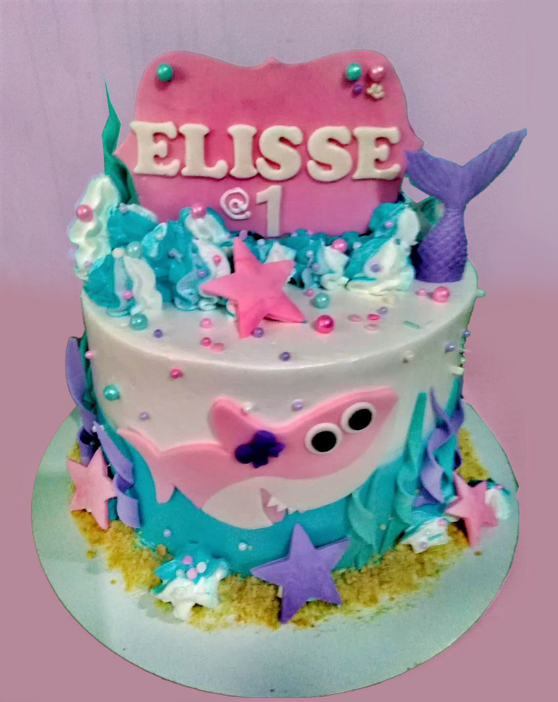 Pink and blue Baby Shark themed birthday cake with a mermaid tail, starfish, and a pink shark fondant figure. Pink and blue Baby Shark themed birthday cake with a mermaid tail, starfish, and a pink shark fondant figure.