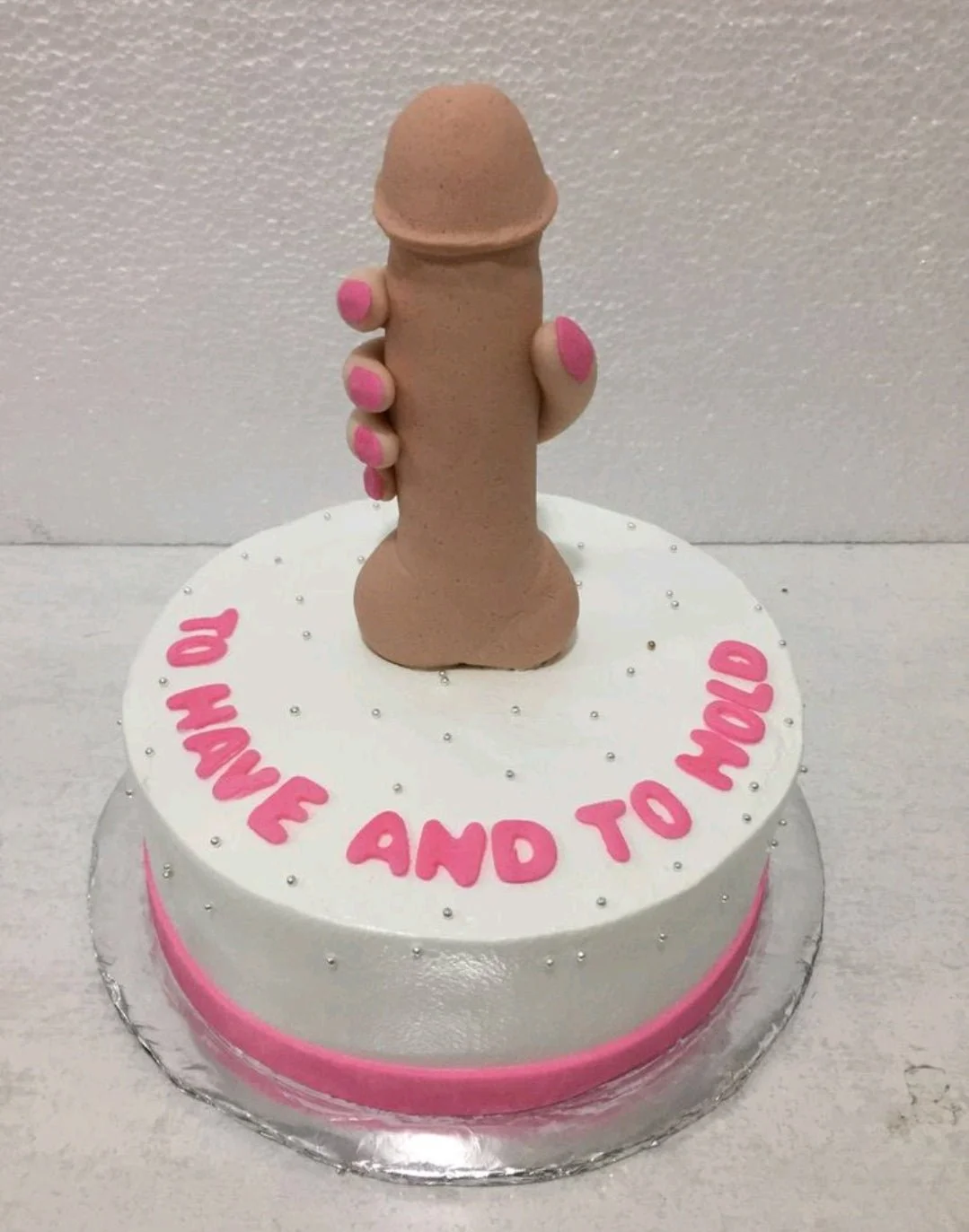 Bachelorette White Cake A white 1 Tier Bachelorette cake with a 3D fondant hand holding a phallic shape, pink text, and silver dragees.