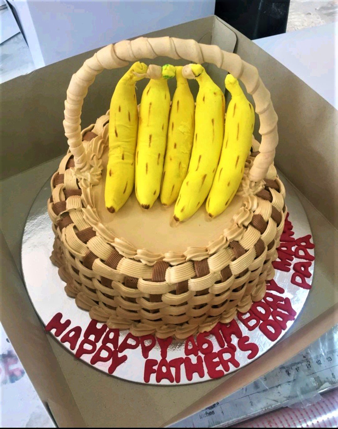 A basket-themed cake with a woven icing design, topped with five yellow fondant bananas and a gumpaste handle. A basket-themed cake with a woven icing design, topped with five yellow fondant bananas and a gumpaste handle.