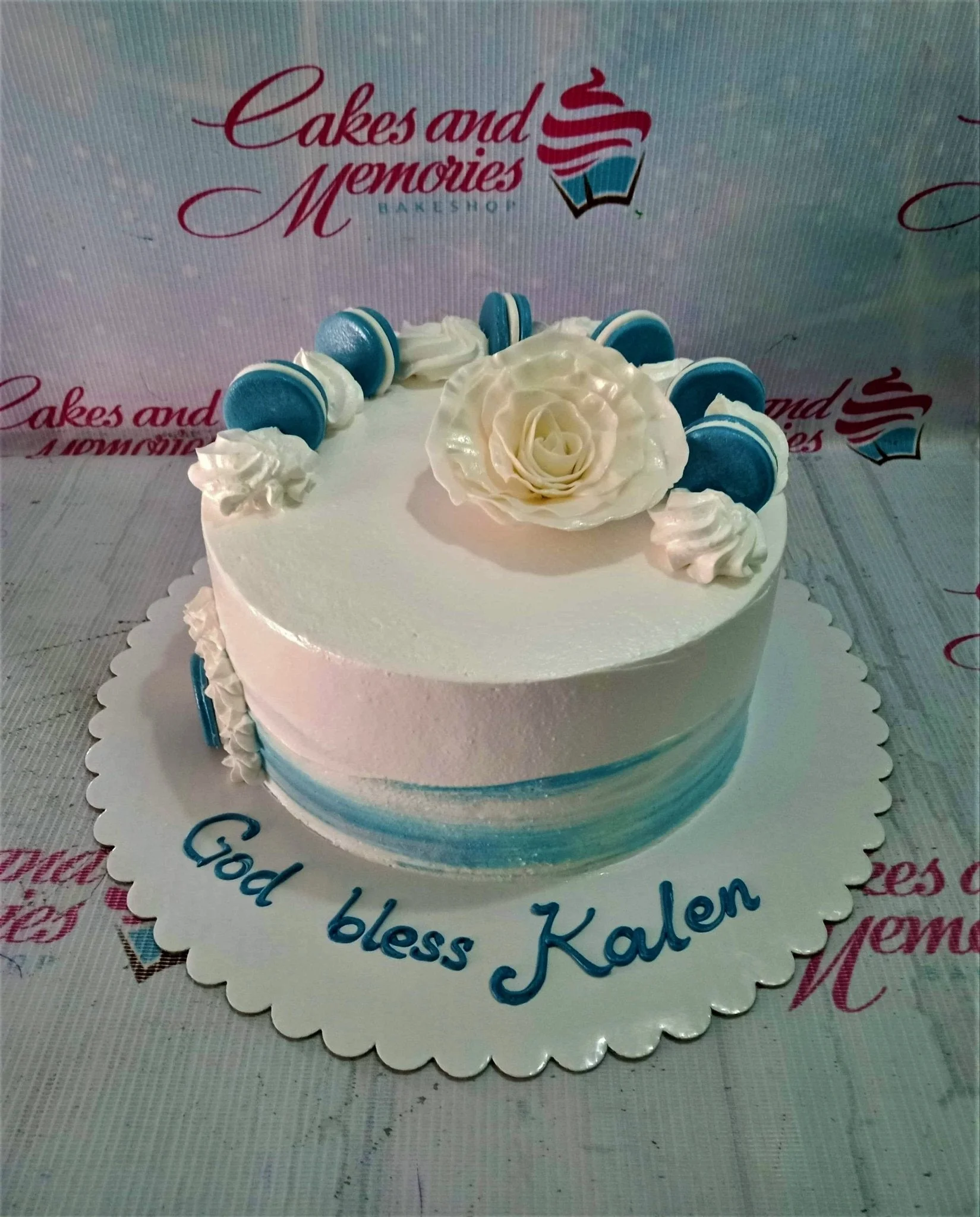 White round cake with blue gradient base, topped with a large white gumpaste rose and blue macarons. White round cake with blue gradient base, topped with a large white gumpaste rose and blue macarons.