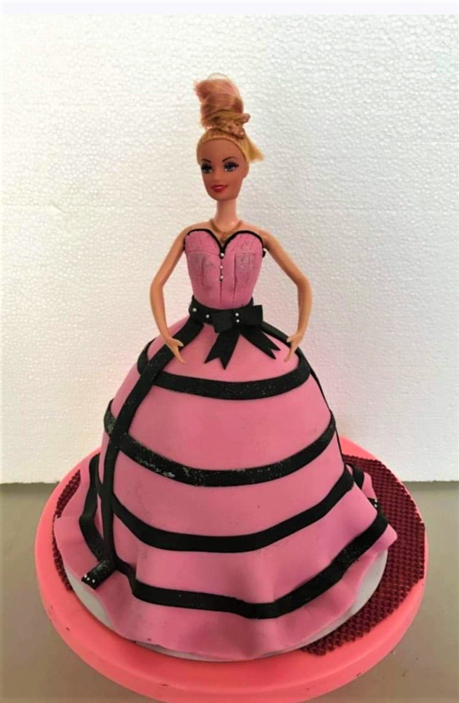 Barbie doll cake with a pink fondant ball gown dress decorated with black glittery stripes and a black bow. Barbie doll cake with a pink fondant ball gown dress decorated with black glittery stripes and a black bow.