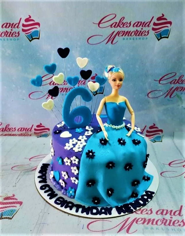 Barbie doll cake with a blue fondant dress and purple base, decorated with white and blue flowers and heart toppers.