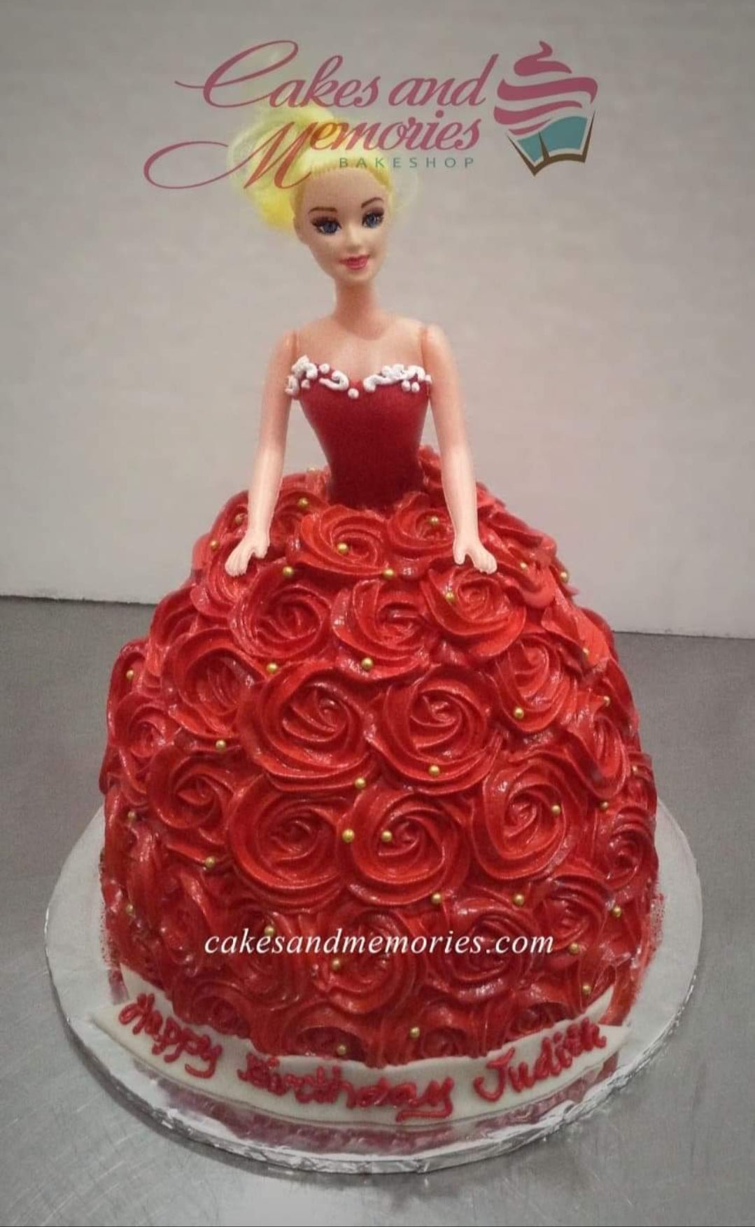 Red Barbie doll cake with a full skirt made of red icing rosettes and gold pearl sprinkles on a white base board. Red Barbie doll cake with a full skirt made of red icing rosettes and gold pearl sprinkles on a white base board.