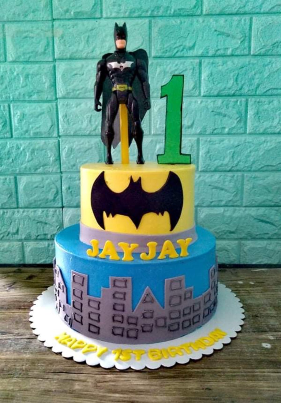 Two-tier Batman themed birthday cake with a Batman action figure topper, city skyline silhouette, and yellow accents. Two-tier Batman themed birthday cake with a Batman action figure topper, city skyline silhouette, and yellow accents.