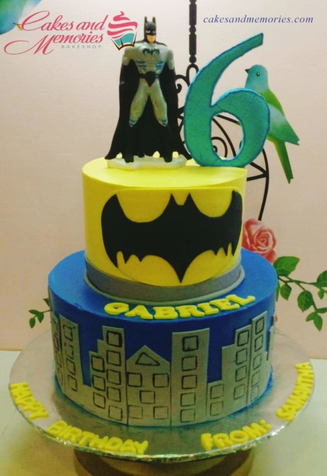 Two-tier Batman themed birthday cake with a yellow top tier featuring the Batman logo and a blue bottom tier with a city skyline. Two-tier Batman themed birthday cake with a yellow top tier featuring the Batman logo and a blue bottom tier with a city skyline.