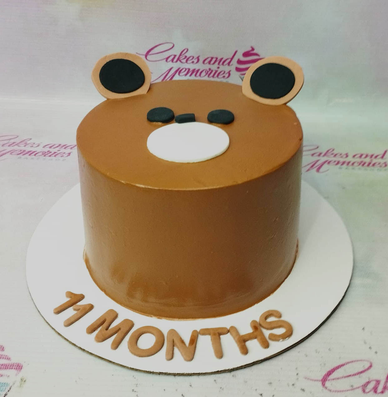 Brown bear face cake with fondant ears and muzzle on a white base board with 11 months message. Brown bear face cake with fondant ears and muzzle on a white base board with 11 months message.