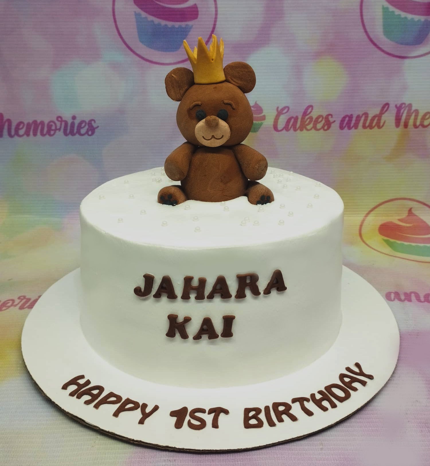 White minimalist birthday cake with a brown fondant bear wearing a gold crown and brown gumpaste letters. White minimalist birthday cake with a brown fondant bear wearing a gold crown and brown gumpaste letters.
