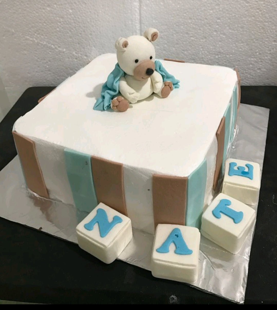 White square fondant cake with blue and brown vertical stripes featuring a 3D fondant bear topper and letter blocks spelling NATE. White square fondant cake with blue and brown vertical stripes featuring a 3D fondant bear topper and letter blocks spelling NATE.