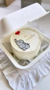 A white Bento cake themed around an 11-month milestone, featuring a grey elephant printout and a red heart. A white Bento cake themed around an 11-month milestone, featuring a grey elephant printout and a red heart.