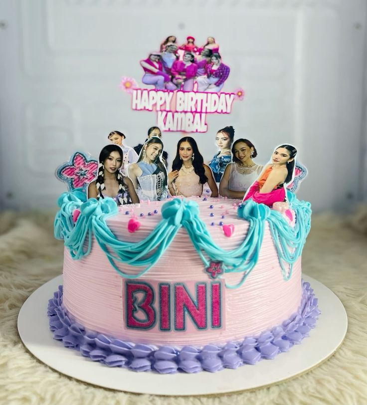 A pink 1 tier cake featuring BINI members printouts, 'Happy Birthday Kambal' message, purple candy beads, fondant hearts and blue icing decorations. A pink 1 tier cake featuring BINI members printouts, 'Happy Birthday Kambal' message, purple candy beads, fondant hearts and blue icing decorations.