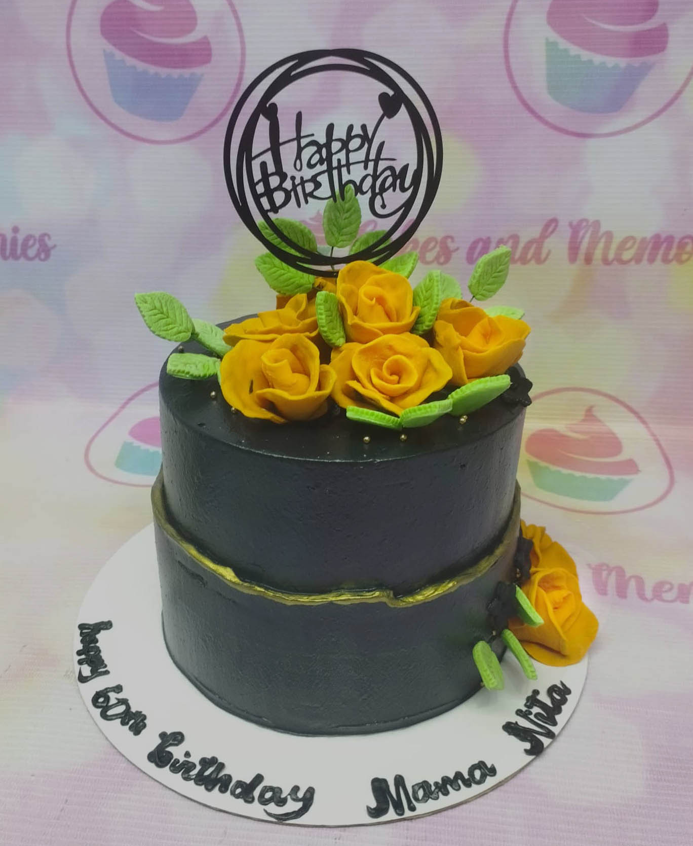 Two-tier black birthday cake with yellow gumpaste roses, green leaves, and a black Happy Birthday topper. Two-tier black birthday cake with yellow gumpaste roses, green leaves, and a black Happy Birthday topper.