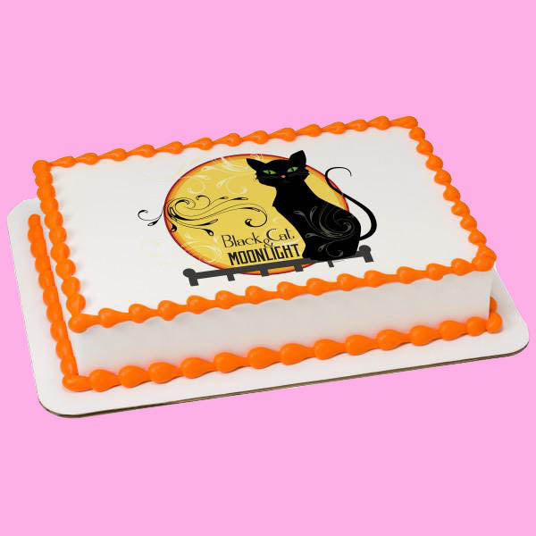 Rectangle white cake with orange icing borders and a black cat sitting in front of a yellow moon printout. Rectangle white cake with orange icing borders and a black cat sitting in front of a yellow moon printout.