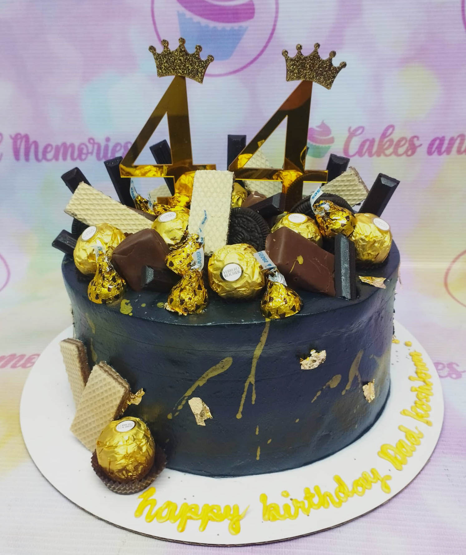 Black chocolate-themed birthday cake with gold number 44 toppers, Ferrero Rocher, and chocolate bars. Black chocolate-themed birthday cake with gold number 44 toppers, Ferrero Rocher, and chocolate bars.