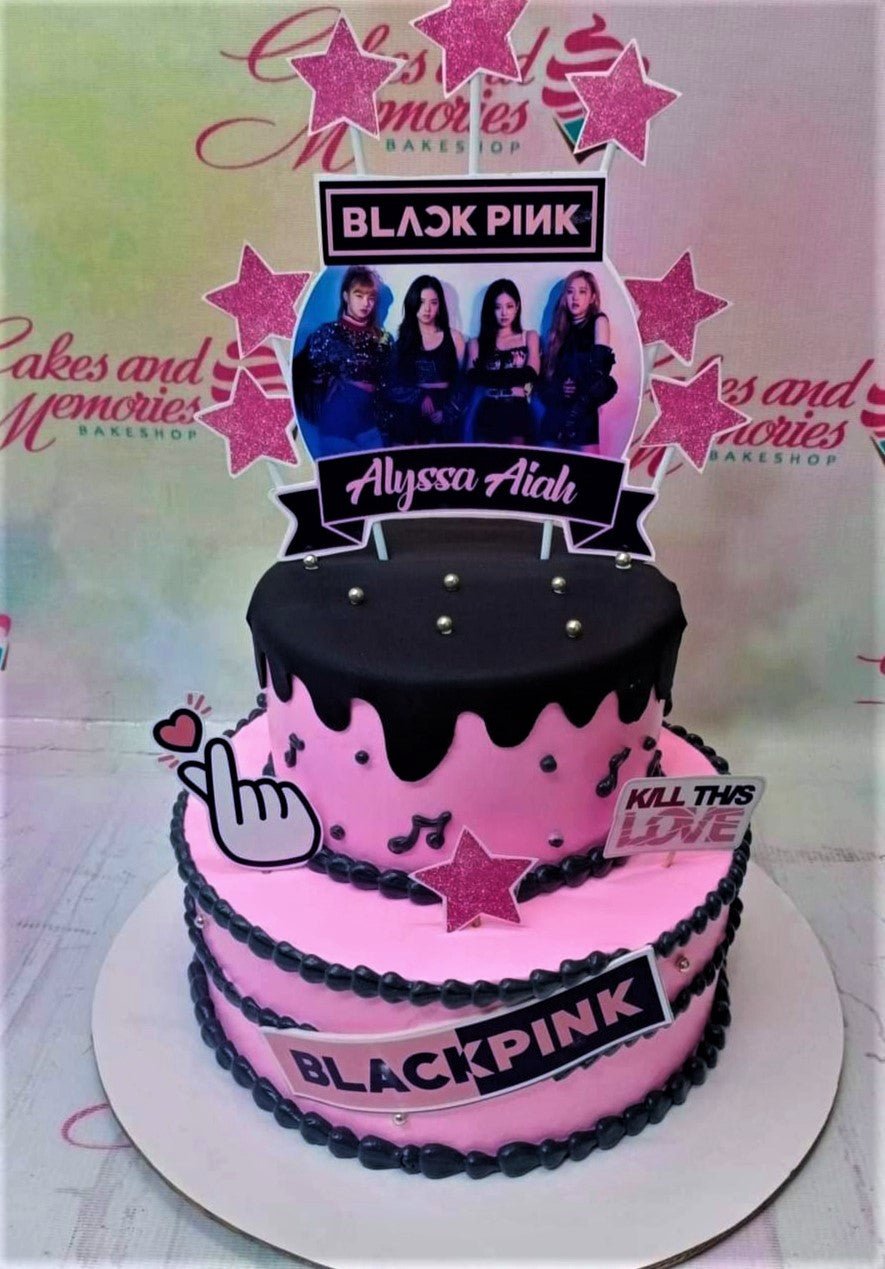 Two-tier pink and black Blackpink themed cake with character printouts, glitter stars, and black icing drip. Two-tier pink and black Blackpink themed cake with character printouts, glitter stars, and black icing drip.