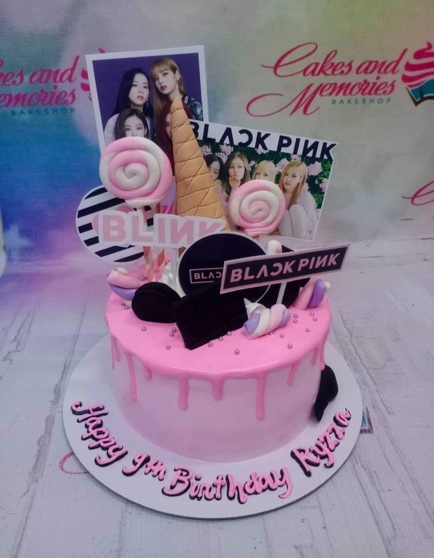 Pink Blackpink themed birthday cake with photo printouts of the K-pop group, lollipops, and a pink drip on a white base board. Pink Blackpink themed birthday cake with photo printouts of the K-pop group, lollipops, and a pink drip on a white base board.