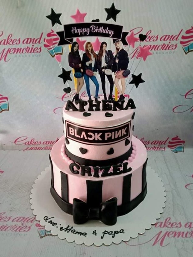Two-tier pink and black Blackpink themed birthday cake with character printouts, stars, and a large black bow. Two-tier pink and black Blackpink themed birthday cake with character printouts, stars, and a large black bow.