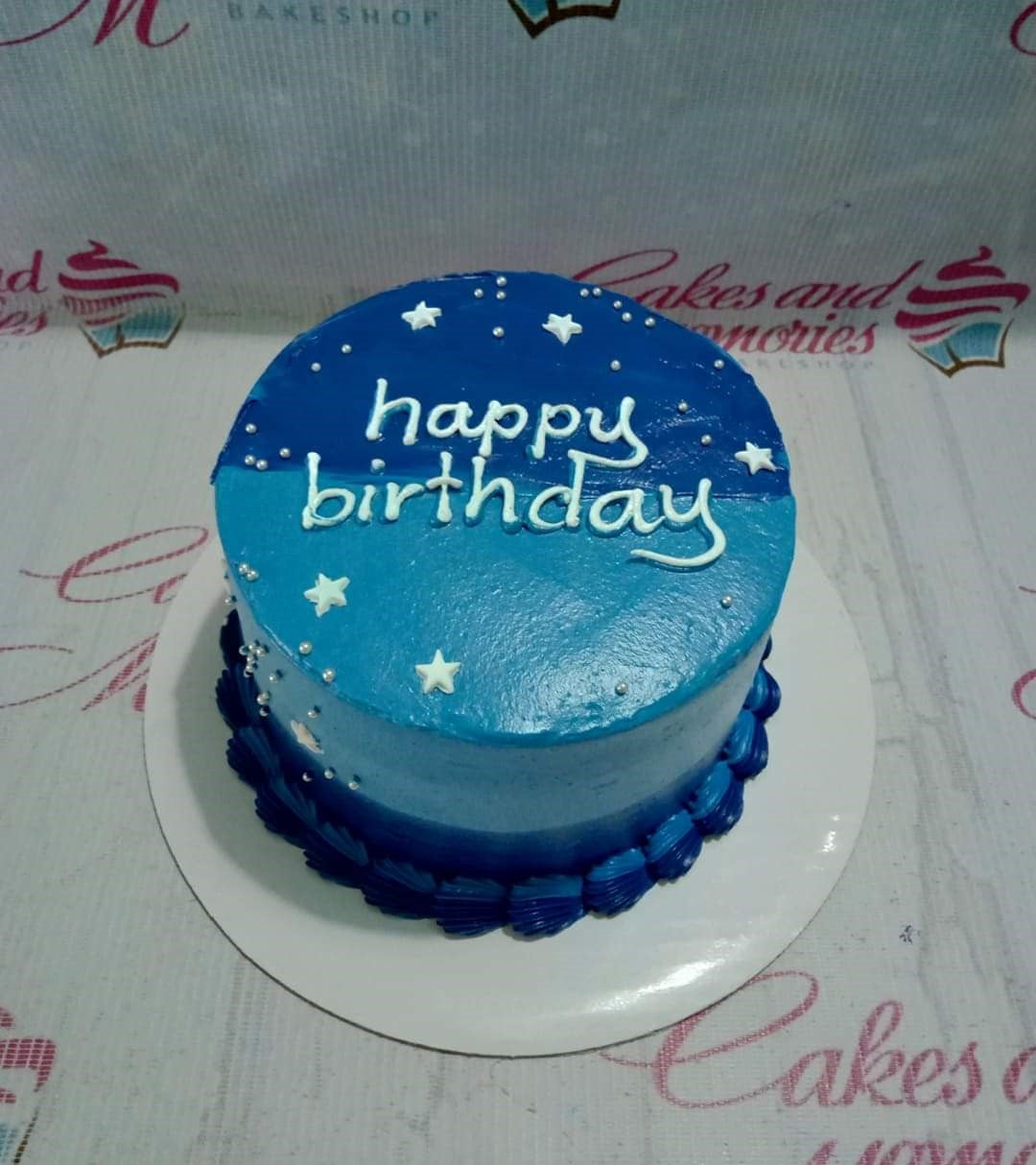 A single-tier blue minimalist birthday cake with white icing stars, silver dragees, and a dark blue shell border. A single-tier blue minimalist birthday cake with white icing stars, silver dragees, and a dark blue shell border.