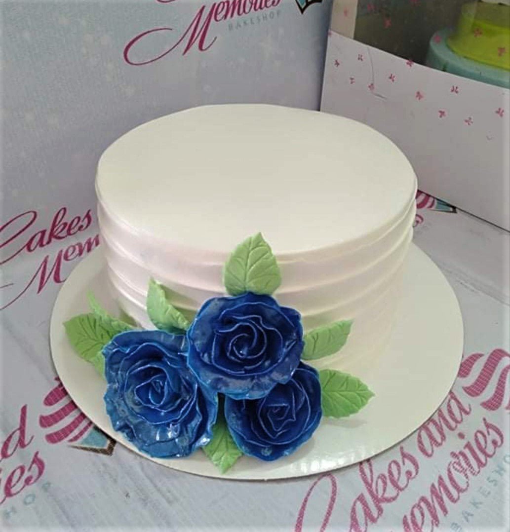 White minimalist cake with horizontal icing ridges and three large blue gumpaste roses with green leaves on the side. White minimalist cake with horizontal icing ridges and three large blue gumpaste roses with green leaves on the side.
