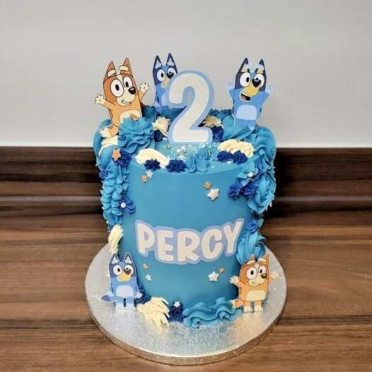 Bluey themed light blue birthday cake with Bluey and Bingo character toppers, blue icing swirls, and white stars. Bluey themed light blue birthday cake with Bluey and Bingo character toppers, blue icing swirls, and white stars.
