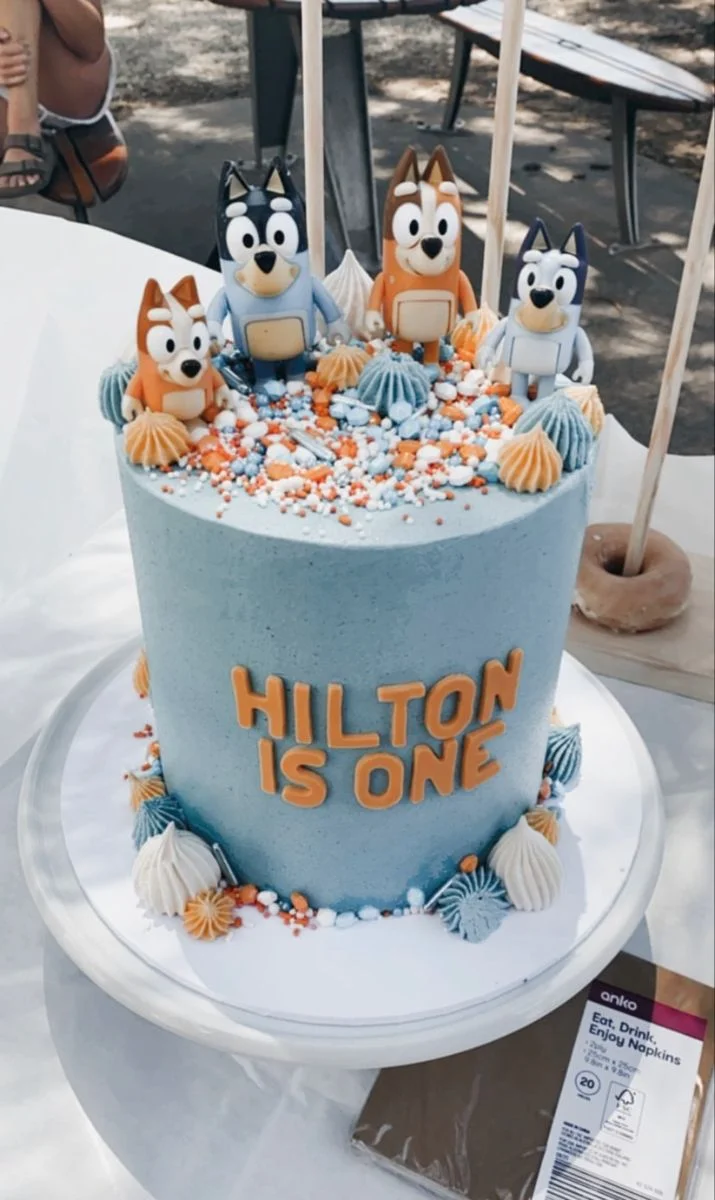 Light blue Bluey themed birthday cake with 3D character figures, orange and blue icing dollops, and colorful sprinkles. Light blue Bluey themed birthday cake with 3D character figures, orange and blue icing dollops, and colorful sprinkles.