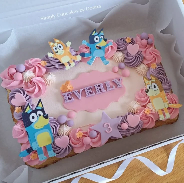 Bluey themed rectangle cake with pink and purple icing rosettes, character printouts, and a pink fondant name plaque for Everly. Bluey themed rectangle cake with pink and purple icing rosettes, character printouts, and a pink fondant name plaque for Everly.