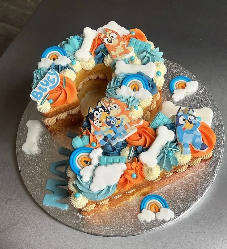 Bluey themed number 2 shaped cake with orange and blue icing rosettes, bone toppers, and character printouts. Bluey themed number 2 shaped cake with orange and blue icing rosettes, bone toppers, and character printouts.