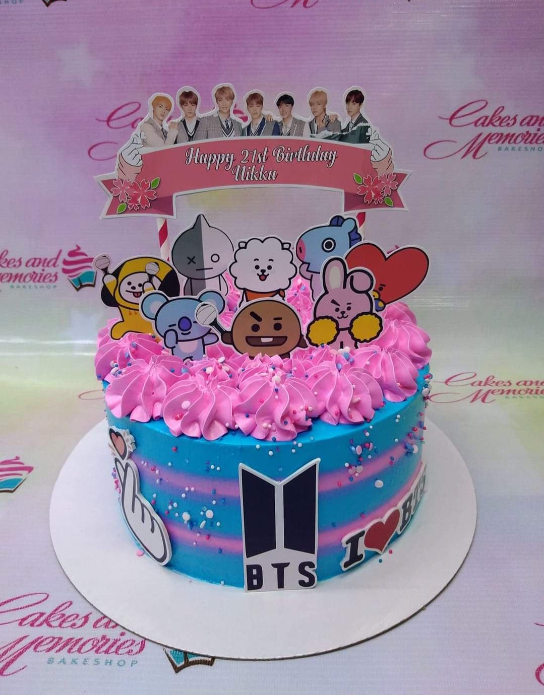 BTS K-pop themed birthday cake with pink icing swirls, blue and pink gradient sides, and various character printouts. BTS K-pop themed birthday cake with pink icing swirls, blue and pink gradient sides, and various character printouts.