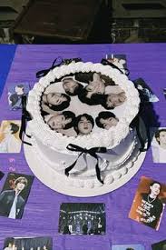White round cake with a printed photo of a K-pop group on top, decorated with white icing rosettes and black ribbons. White round cake with a printed photo of a K-pop group on top, decorated with white icing rosettes and black ribbons.