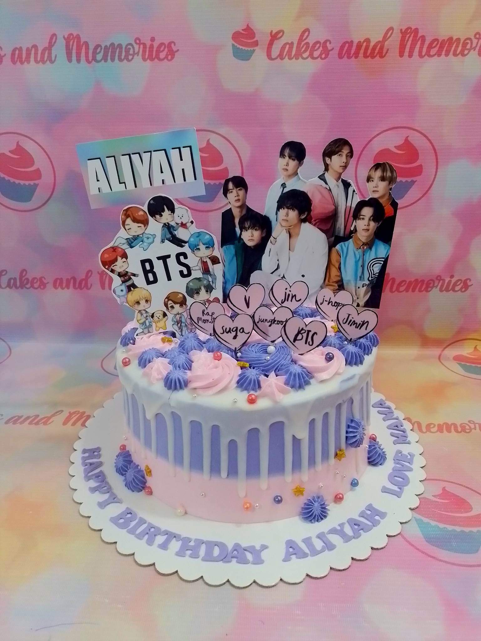 BTS themed birthday cake with purple and pink icing, character printouts, and a white drip effect. BTS themed birthday cake with purple and pink icing, character printouts, and a white drip effect.