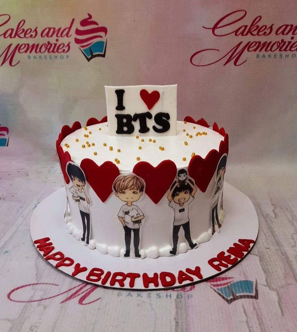 White BTS themed birthday cake with red heart cutouts, cartoon character printouts, and gold sprinkles. White BTS themed birthday cake with red heart cutouts, cartoon character printouts, and gold sprinkles.