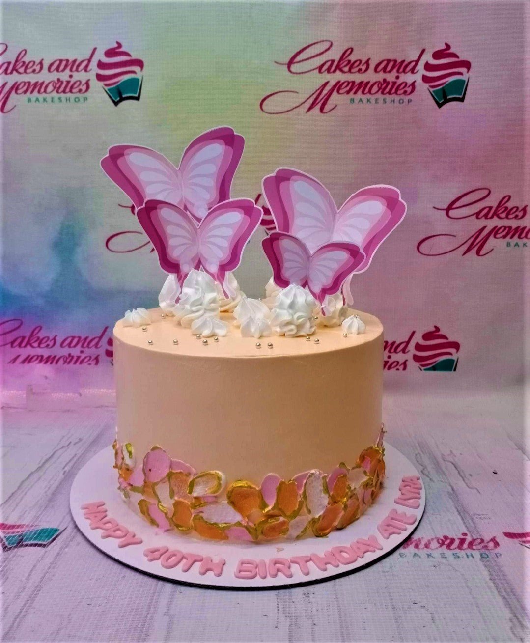 Peach-colored single tier birthday cake with large pink butterfly printouts, white icing dollops, and palette knife floral textures.