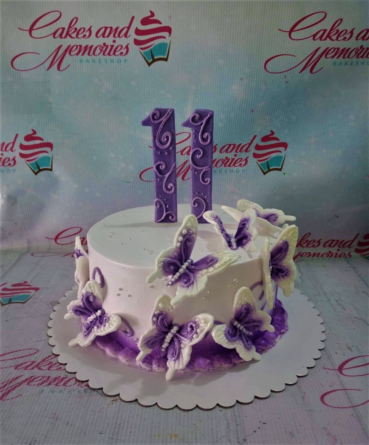White 1-tier birthday cake decorated with purple and white fondant butterflies and large purple number 11 toppers. White 1-tier birthday cake decorated with purple and white fondant butterflies and large purple number 11 toppers.