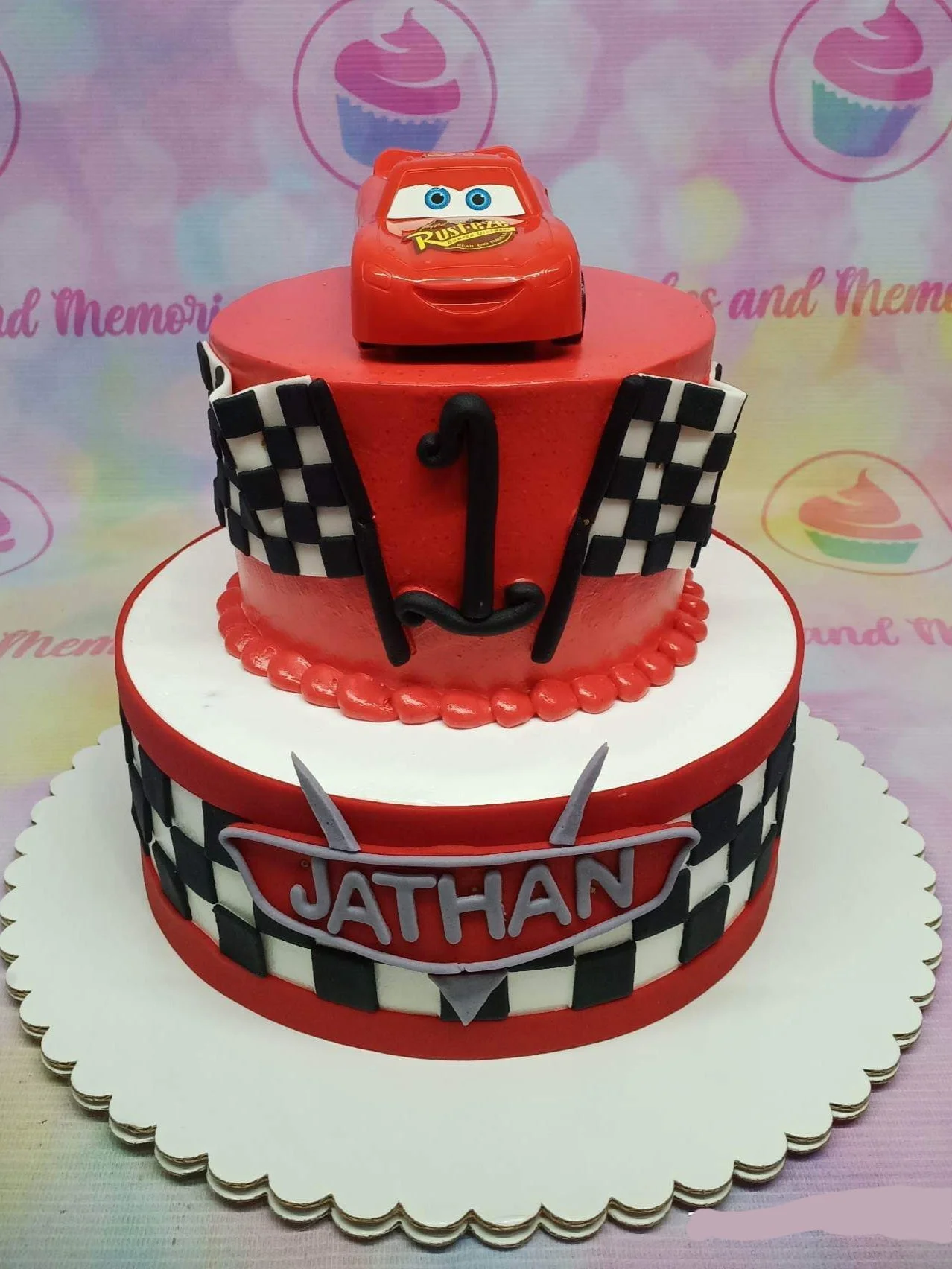 Cars Lightning McQueen-Inspired 2-Tier Cake Two-tier Disney Cars themed cake featuring Lightning McQueen toy topper, checkered flags, and a custom Jathan nameplate.