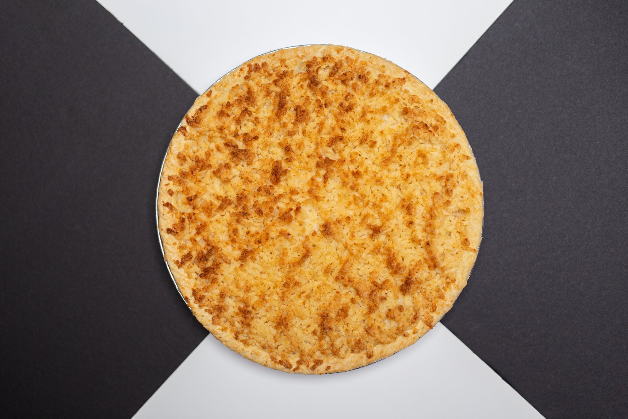 Top-down view of a round cassava cake or bibingka with a golden-brown toasted cheese and coconut topping in a silver foil tray. Top-down view of a round cassava cake or bibingka with a golden-brown toasted cheese and coconut topping in a silver foil tray.