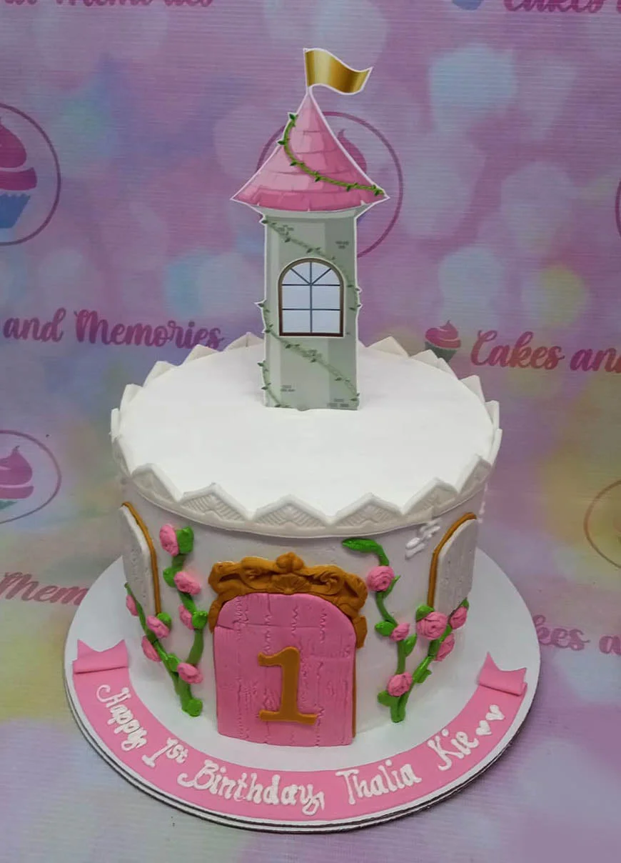A white and pink 1 Tier Fondant cake themed around a castle, featuring a castle tower topper, pink door, gold number one, and pink roses with green vines. A white and pink 1 Tier Fondant cake themed around a castle, featuring a castle tower topper, pink door, gold number one, and pink roses with green vines.