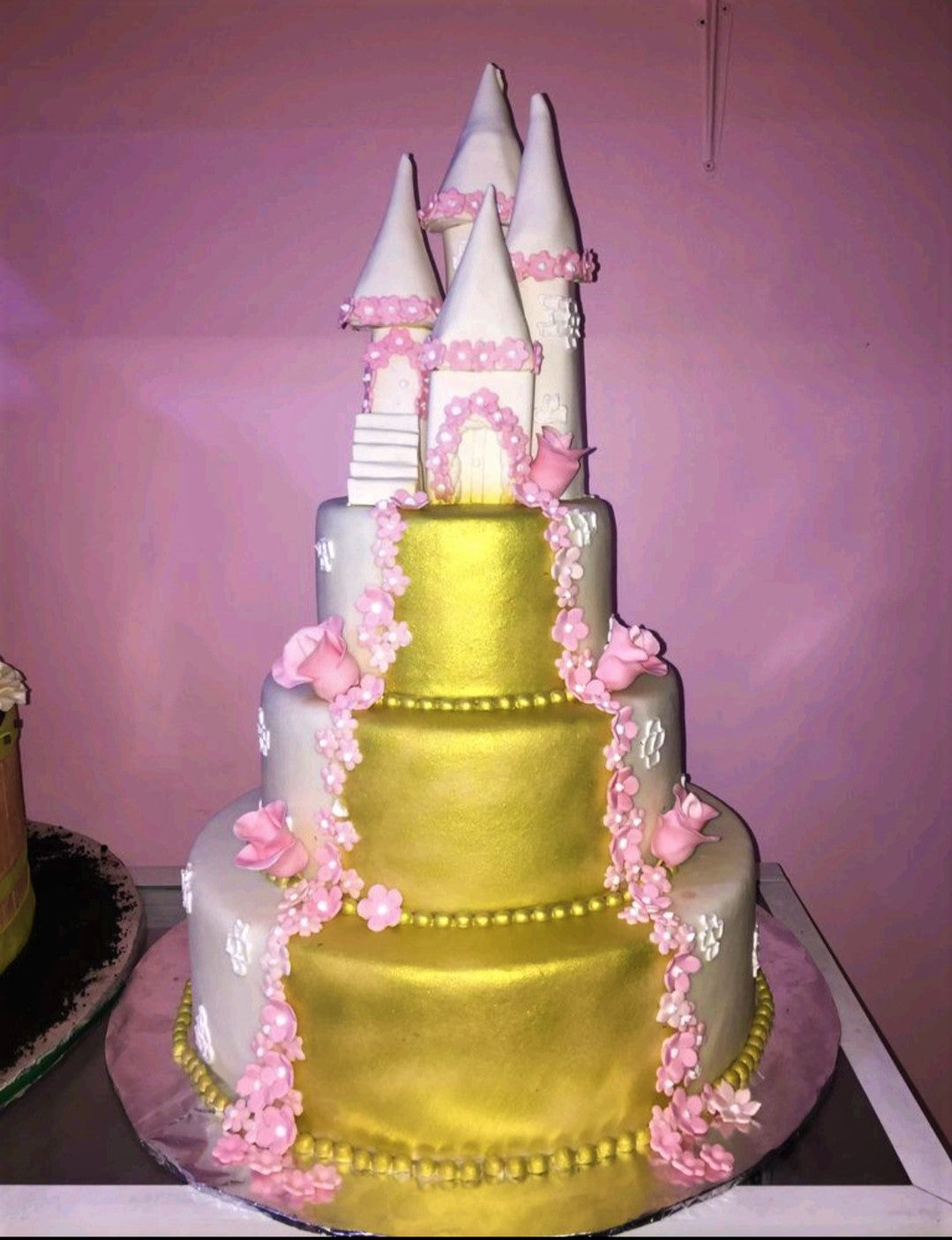 Three-tier gold and white castle cake with pink fondant flowers and a large fondant castle topper. Three-tier gold and white castle cake with pink fondant flowers and a large fondant castle topper.