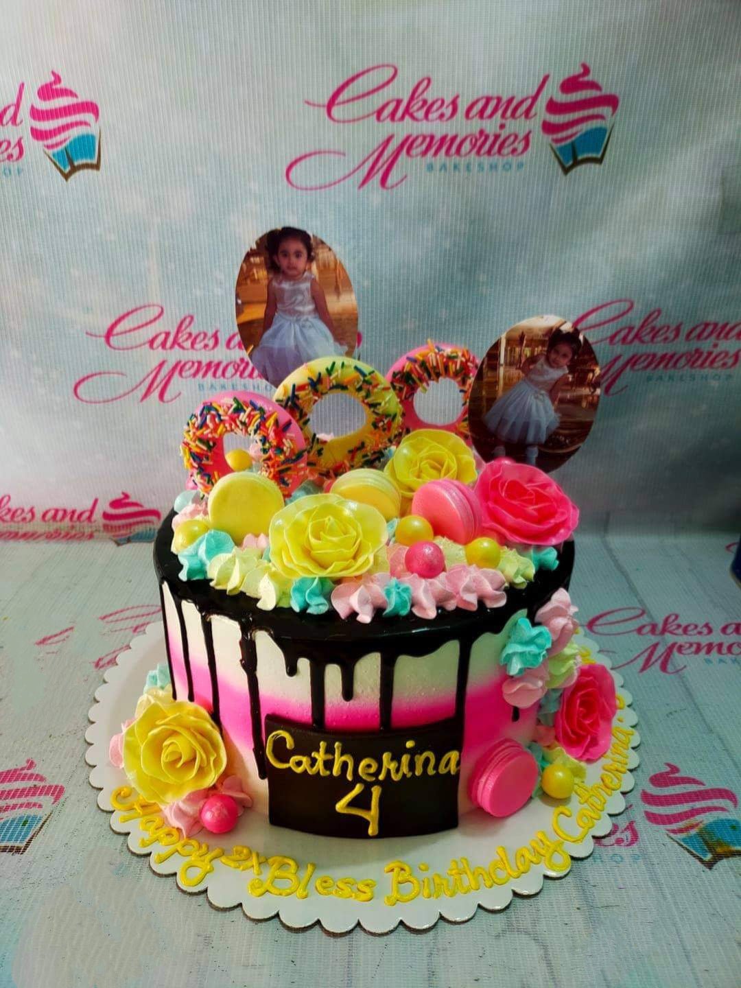 Colorful 1-tier birthday cake with pink and teal gradient icing, chocolate drip, donuts, macarons, and photo printouts of a young girl. Colorful 1-tier birthday cake with pink and teal gradient icing, chocolate drip, donuts, macarons, and photo printouts of a young girl.