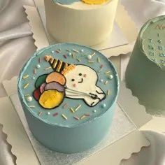 Light blue bento cake with a hand-drawn icing doodle of a character wearing a party hat and holding colorful balloons. Light blue bento cake with a hand-drawn icing doodle of a character wearing a party hat and holding colorful balloons.